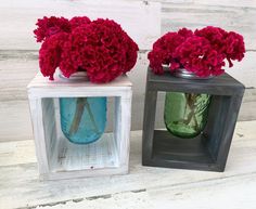 two vases with red flowers in them on a white wooden table next to each other