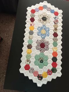 a quilted table runner made out of hexagons and buttons on a black surface