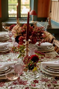 the table is set with red flowers and white plates, silverware and candlesticks