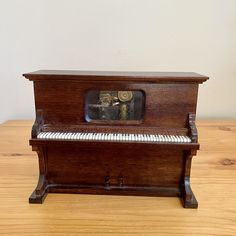 an old wooden piano sitting on top of a wooden table next to a white wall