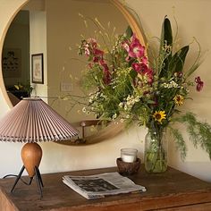 a vase filled with flowers sitting on top of a wooden table next to a mirror