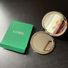 a compact mirror sitting on top of a table next to a green box with the word la mer written on it