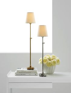 two lamps sitting on top of a white table next to a vase filled with flowers