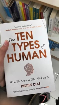 a person holding up a book in front of a bookshelf