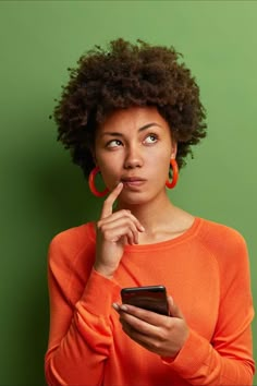 a woman holding a cell phone and looking at her finger on her lips while standing in front of a green wall