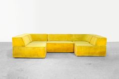 a yellow sectional couch sitting on top of a cement floor next to a white wall