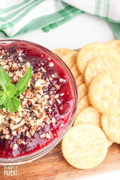 a bowl of cranberry sauce next to crackers on a wooden cutting board