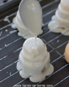 a spoon pouring white icing onto some pastries