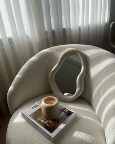 a candle sitting on top of a white chair next to a magazine and a window