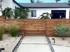 a wooden fence in front of a house with gravel and plants on the ground next to it