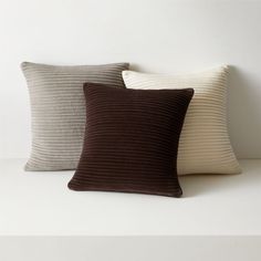 three pillows sitting next to each other on top of a white table with a black and brown pillow