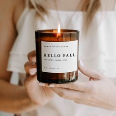 a woman holding a candle in her hands with the words hello fall printed on it