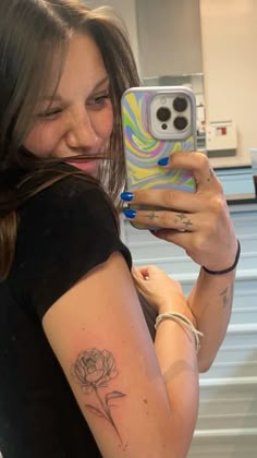 a woman taking a selfie with her cell phone and flower tattoo on her arm