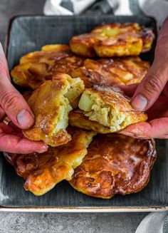 two hands holding up some food on top of a pan filled with pastries and sauces