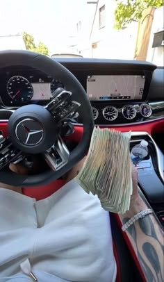 a man driving a car with cash in his hand and the steering wheel is shown