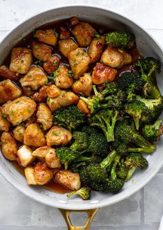 chicken and broccoli in a skillet on a white counter top with gold spoons