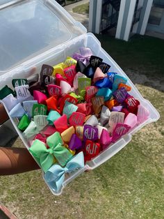 a person holding a container filled with lots of small colorful bow ties in it's hands