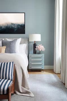 a bedroom with blue walls and white bedding, striped pillows, and a painting on the wall