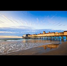 a long pier sitting on top of a sandy beach next to the ocean under a blue cloudy sky