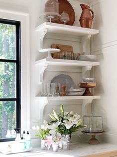 a kitchen with white walls and shelves filled with dishes, cups and vases on top of them