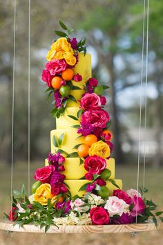 a tall yellow cake with flowers and oranges on the top is suspended by strings