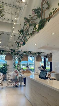 people sitting at tables in a restaurant with plants growing on the ceiling and windows above them