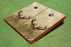 a cornhole game with two deer antlers on the side and grass in front