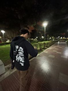 a man walking down a sidewalk at night with his back to the camera and lights on