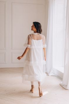 a woman standing in front of a window wearing a white dress with sheer sleeves and high heels