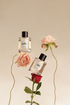 two perfume bottles sitting next to each other on top of a vase with flowers in it