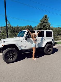 a woman standing in front of a white jeep with her arms up and hands on the door