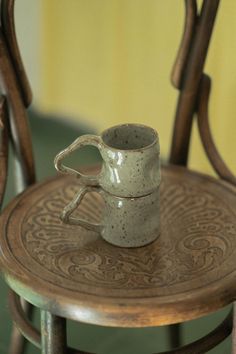 a small cup sitting on top of a wooden table next to a chair with two legs