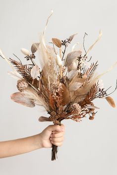 a person holding a bunch of dried flowers in their hand with the stems sprouting out