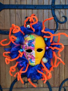 a colorful mask hanging on the side of a wooden door with blue and orange streamers