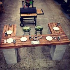 a wooden table topped with white plates and silverware next to an outdoor bbq