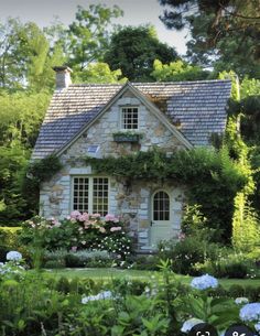 an old stone house surrounded by flowers and greenery