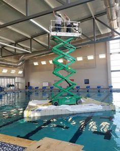 a man standing on top of a lift in a swimming pool next to a ladder