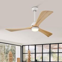 a ceiling fan with wooden blades in a living room next to large windows and potted plants