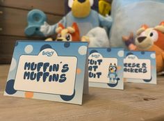 two stuffed animals sitting next to each other on top of a wooden table with signs that say muffin's muffins out