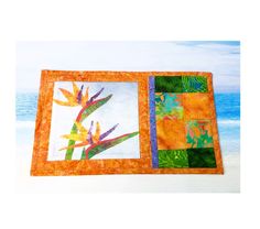 an orange and green quilted placemat with flowers on the beach in the background