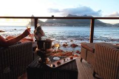 two people sitting on chairs with drinks in front of the ocean and mountains behind them