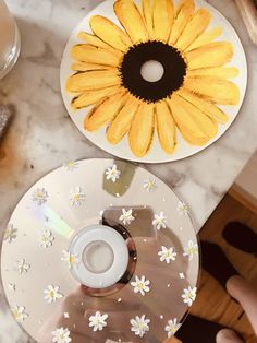 someone holding a cd in front of a yellow flower on a white plate with black center