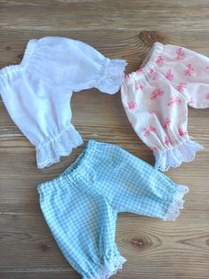 three baby doll clothes laying on top of a wooden floor next to an adult doll