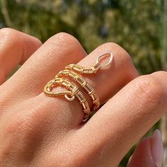 a woman's hand holding a gold ring with three loops on the middle of it