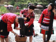 three women in traditional dress are washing the water from a wooden barrel while another woman looks on