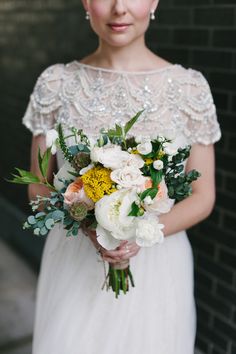 a woman in a white dress holding a bouquet of flowers and looking at the camera