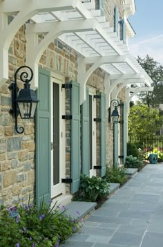 the front entrance to a house with green shutters and blue doors, surrounded by flowers