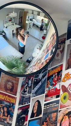 a woman taking a selfie in front of a mirror with posters on the wall