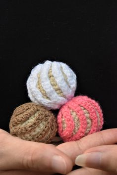 three small crocheted balls in the palm of someone's hand on a black background