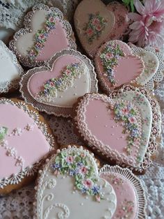 several decorated heart shaped cookies on a lace doily with pink flowers in the background